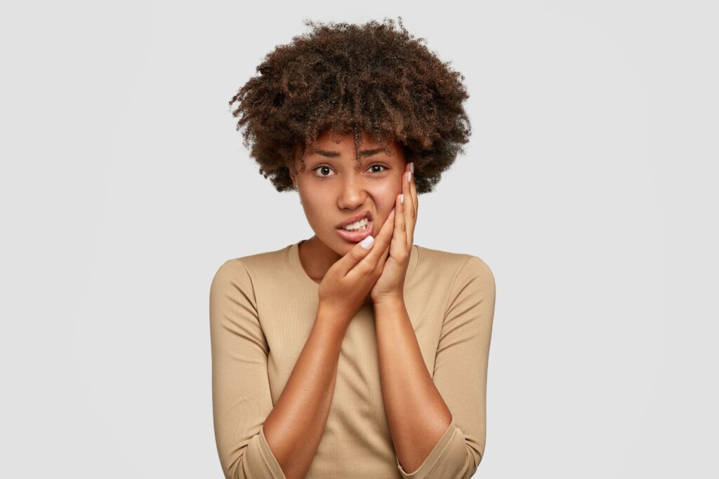 Woman in brown shirt holding hands to the side of her face in pain